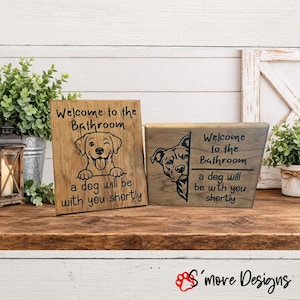 May include: Two rectangular wooden signs with dark brown text and dog illustrations. The left sign reads Welcome to the Bathroom a dog will be with you shortly with a winking dog. The right sign features a dog peeking out with the same text.