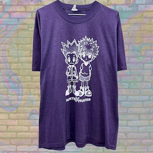 May include: Purple t-shirt with a white graphic print of two cartoon characters from the anime Hunter x Hunter. The characters are Gon Freecs and Killua Zoldyck. The text "HUNTER x HUNTER" is printed below the characters.