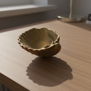 Puede incluir: Un pequeño cuenco decorativo de latón con diseño de concha. El cuenco tiene una superficie texturizada y un borde ondulado. Está sobre una superficie de madera, proyectando una sombra.