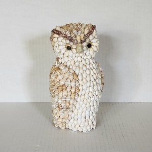 May include: A white owl figurine made entirely of small seashells. The owl has brown eyes and a brown beak.