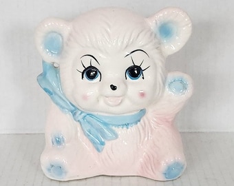 May include: A pink ceramic bear figurine with blue eyes, a blue bow, and blue accents on its paws.