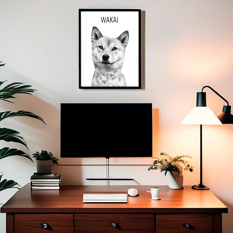 May include: Black and white illustration of a Shiba Inu dog with the name "Wakai" printed above the dog. The illustration is framed and hanging on a white wall above a desk with a computer monitor, a keyboard, a lamp, and plants.