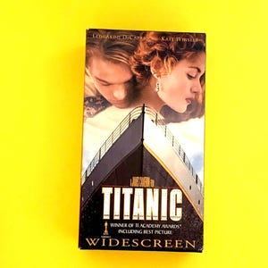 Può includere: Una videocassetta VHS del film "Titanic" con Leonardo DiCaprio e Kate Winslet. La copertina mostra la prua della nave e il titolo del film in lettere bianche. Il nastro è etichettato "Widescreen".