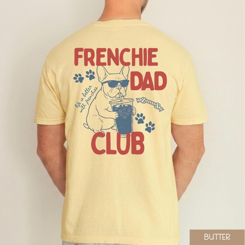 May include: Pale yellow t-shirt featuring a French Bulldog graphic wearing sunglasses and drinking from a cup. The text reads "FRENCHIE DAD CLUB" in red, with blue paw prints and the phrase "Life is better with frenchies."