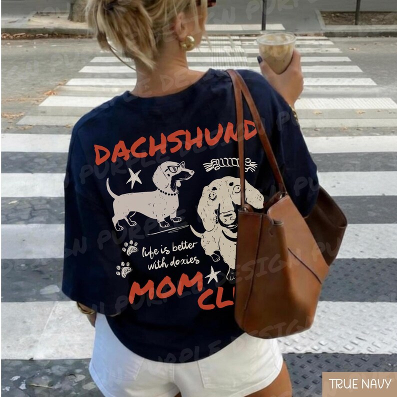 May include: Navy blue t-shirt with a dachshund graphic and the words "DACHSHUND MOM CLUB". The design includes two dachshund illustrations and the phrase "life is better with doxies".