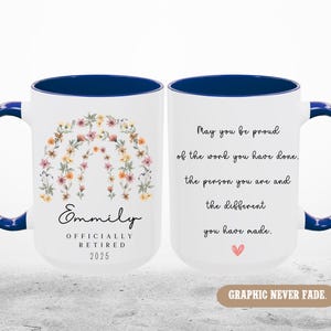 Peut inclure: Une tasse &agrave; caf&eacute; blanche avec un bord et une poign&eacute;e bleus. La tasse pr&eacute;sente un motif floral et le texte "Emmily Officially Retired 2025". L'autre c&ocirc;t&eacute; de la tasse a le texte "May you be proud of the work you have done, the person you are and the different you have made."