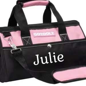 May include: Black and pink tool bag with the name "Julie" in white script. The bag has a shoulder strap and a handle with a pink grip. The brand name "GOTOOLZ" is printed on the front.