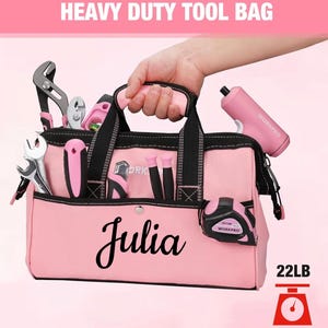 Puede incluir: Bolsa de herramientas rosa resistente con detalles negros, llena de herramientas. La bolsa tiene el nombre "Julia" impreso. Contiene un taladro rosa WORKPRO y una cinta métrica WORKPRO. La bolsa está clasificada para 10 kg.