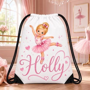 May include: White drawstring backpack featuring a ballerina illustration in a pink tutu and ballet shoes. The name "Holly" is written in pink script. Black drawstrings and accents complete the design. Hearts and stars are scattered around the ballerina.