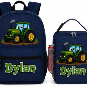 May include: A navy blue backpack and matching lunch bag set, both featuring a cartoon green tractor graphic and the name Dylan printed in large green letters. The backpack has adjustable straps and side mesh pockets, while the lunch bag has a handle.