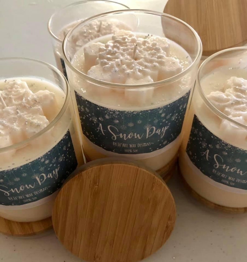 Puede incluir: Cuatro velas de vidrio con tapas de madera. Las velas tienen un dise&ntilde;o de copo de nieve en la parte superior y una etiqueta que dice "A Snow Day". Las velas est&aacute;n hechas de cera cremosa y 100% soja.