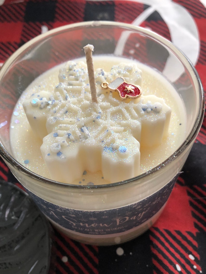 Puede incluir: Vela perfumada "Snow Day" en un tarro de cristal transparente. La vela presenta un dise&ntilde;o de copo de nieve blanco con detalles de purpurina azul y un peque&ntilde;o dije de mit&oacute;n. La vela tiene una mecha.