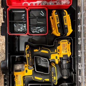 May include: A black and yellow DeWalt power tool kit with a clear lid. The kit contains a drill, impact driver, two 20V batteries, and compartments with screws and other hardware. The tools are black and yellow.