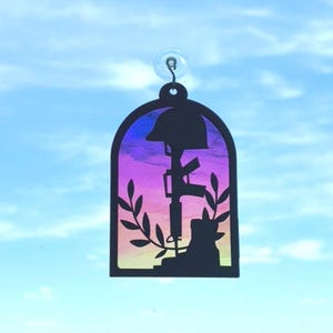 Puede incluir: Un memorial de silueta negra con un casco, un rifle y botas, sobre un fondo de acuarela con tonos morados, rosas y amarillos. El memorial está enmarcado por un arco y sujeto a una ventosa.