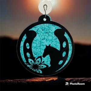May include: A turquoise blue horseshoe ornament with a black silhouette of a horse and a flower. The ornament is hanging from a silver hook.