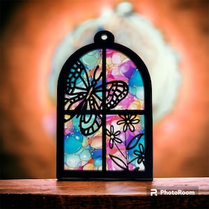 Peut inclure: Un cadre de fenêtre en métal noir avec un motif de vitrail représentant un papillon et des fleurs. Le vitrail est coloré avec des nuances de bleu, rose et violet.