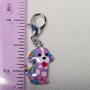Pu&ograve; includere: Un ciondolo a forma di cane viola e bianco con pois colorati e una chiusura argentata. Il ciondolo &egrave; alto circa 2,5 cm.