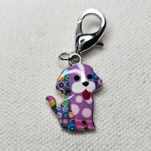Pu&ograve; includere: Un ciondolo a forma di cane argentato con un design a motivi viola, bianco e multicolore. Il ciondolo ha una chiusura girevole argentata.