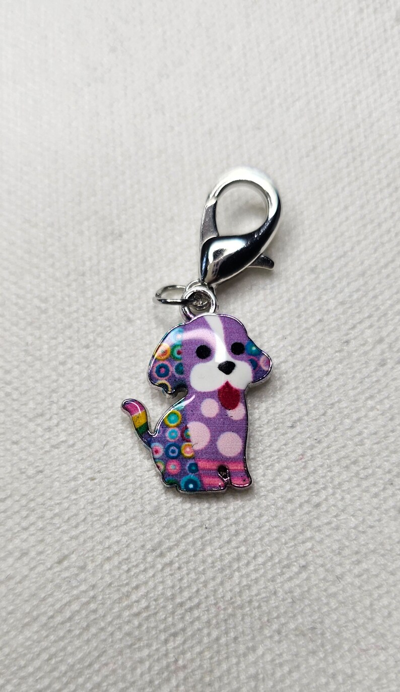 Pu&ograve; includere: Un ciondolo a forma di cane argentato con un design a motivi viola, bianco e multicolore. Il ciondolo ha una chiusura girevole argentata.