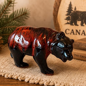 May include: A ceramic bear figurine featuring a glossy finish with a marbled pattern of deep black and vibrant red. The bear is depicted in a standing position with its head slightly lowered, showcasing smooth, reflective surfaces and defined features.