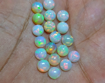 Può includere: Una collezione di opali rotondi e iridescenti. Gli opali mostrano una gamma di colori, tra cui blu, verde, giallo e rosa, con una base bianco latte. Le pietre preziose sono lisce e lucide.