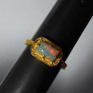 May include: A gold ring featuring a rectangular opal gemstone. The opal displays a mix of colors, including orange and blue. The ring has a textured gold setting and band, showcasing a vintage or handcrafted style.
