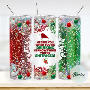 May include: Three Christmas-themed glitter tumblers with red, green, and white glitter. The center tumbler has a white background with a Santa hat and the text "He sees you when you're drinking, he knows when you're shitfaced!"
