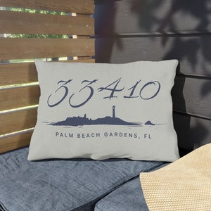May include: A white throw pillow with a navy blue design featuring the number 33410 and the text "Palm Beach Gardens, FL".