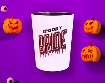 May include: White ceramic mug with a black rim and handle. The mug features a graphic of the text "SPOOKY BRIDE" in red and orange with dripping blood. The mug is surrounded by Halloween decorations, including pumpkins, spiders, and eyeballs.