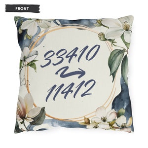 Peut inclure: Un coussin blanc avec un motif circulaire doré et des accents bleus en aquarelle. Le cercle contient les nombres 33410 et 11412 avec une flèche pointant du premier nombre vers le second. Le coussin est décoré de fleurs blanches et de feuilles vertes.