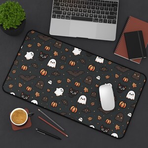Peut inclure: Un tapis de souris noir et blanc sur le thème d'Halloween avec un motif répétitif de fantômes, de chauves-souris, de citrouilles et de chats noirs. Le tapis de souris est sur une surface noire avec un ordinateur portable, une tasse à café et des crayons.