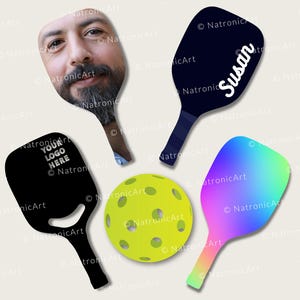 Könnte beinhalten: Eine Auswahl an Pickleball-Schlägern und ein gelber Ball. Schläger zeigen ein Gesicht, den Namen "Susan", einen Platz für ein Logo und einen Regenbogenverlauf. Der Ball ist gelb mit gleichmäßig verteilten Löchern.