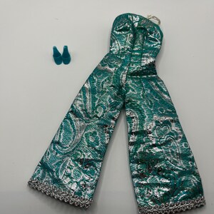 May include: A strapless jumpsuit in a vibrant teal and metallic silver paisley pattern, featuring wide-leg trousers with a silver braided trim at the hem, accompanied by a pair of small, solid teal pointed-toe shoes for a doll.