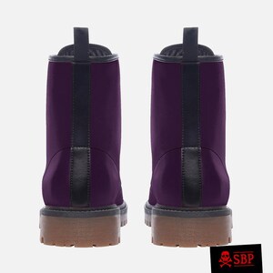 Pu&ograve; includere: Un paio di stivali da combattimento viola con dettagli neri e suole marroni. Gli stivali hanno un design classico. L'immagine include un logo nell'angolo in basso a destra. Calzature eleganti.