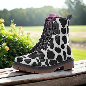 May include: Black and white cow print lace-up boots with a pink skull and crossbones design on the top of the boot.