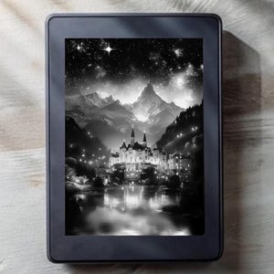 May include: A black and white e-reader displays a scenic illustration of a castle by a lake, with mountains and a starry night sky in the background. The e-reader is rectangular and rests on a light-colored wooden surface.