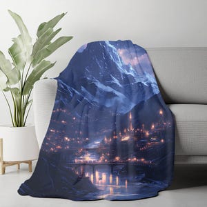 May include: A plush throw blanket draped over a sofa, featuring a digital art print of a mountain range and a city at night. The artwork showcases a river, bridges, and illuminated buildings in shades of blue, purple, and gold.