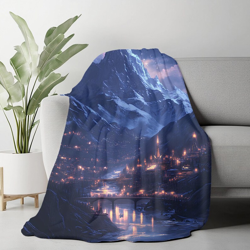 May include: A plush throw blanket draped over a sofa, featuring a digital art print of a mountain range and a city at night. The artwork showcases a river, bridges, and illuminated buildings in shades of blue, purple, and gold.