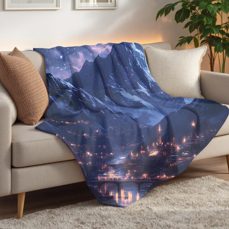 May include: A blue and white throw blanket featuring a fantasy landscape with mountains, a city, and a starry sky. The blanket is draped over a beige sofa, creating a cozy and inviting atmosphere.