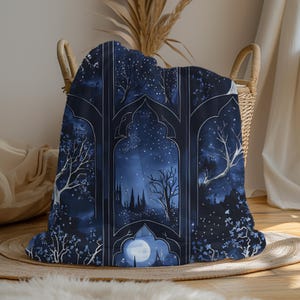 May include: A dark blue throw blanket with a nighttime landscape design. The blanket features a starry sky, trees, and a full moon, framed by arched window-like borders. The design is in shades of blue and white.