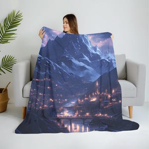 May include: A plush blanket featuring a detailed illustration of a mountain range at dusk. The artwork depicts a city with illuminated buildings, a bridge, and a river, all under a starry sky. The color palette includes shades of blue, purple, and orange.