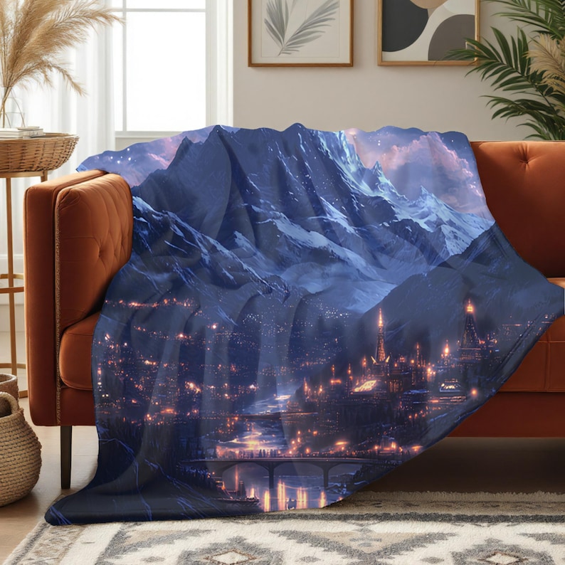 May include: A dark blue blanket featuring a mountain landscape with a city at the base. The blanket has a detailed illustration of a mountain range, a city with illuminated buildings, and a bridge.