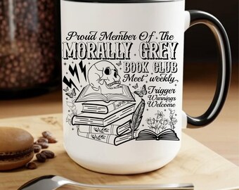 Può includere: Una tazza in ceramica bianca con bordo e manico neri. La tazza presenta un'illustrazione in bianco e nero di uno scheletro, libri e una penna. Il testo sulla tazza recita "Proud Member of the Morally Grey Book Club Meet weekly Trigger Warnings Welcome".