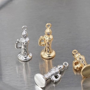 Puede incluir: Primer plano de cuatro pequeños colgantes decorativos con forma de cáliz. Dos son plateados y dos dorados. Cada colgante tiene un asa y un lazo para sujetarlo a una joya.