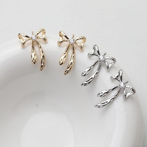 May include: Two pairs of earrings with a bow design. One pair is gold and the other is silver.