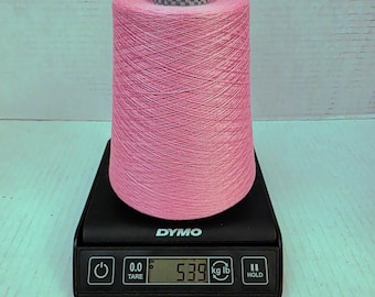 May include: A large spool of pink yarn is on a black digital scale. The scale shows a weight of 2.44 kg. The yarn is tightly wound and has a checkered pattern at the top. The scale is a DYMO brand.