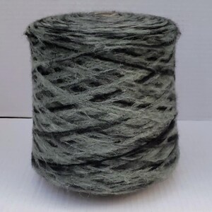 May include: A skein of yarn in a dark green and black colourway. The yarn is a blend of wool and mohair, giving it a soft and fuzzy texture.