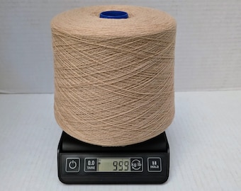 May include: A large cylindrical spool of light beige yarn with a blue plastic centre core, resting on a black digital scale that displays a weight of 999 kg. The yarn is tightly wound in a cross-hatch pattern around the central spool.