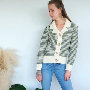 Weibliches Model trägt Strickjacke in creme,Bündchen und Kragen in creme. Rest grün gestreift. Dazu trägt sie eine hellblaue Jeans und weiße Sneaker.