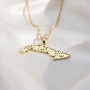 A gold-colored pendant necklace with a map of Cuba on it, resting on a white fabric background.